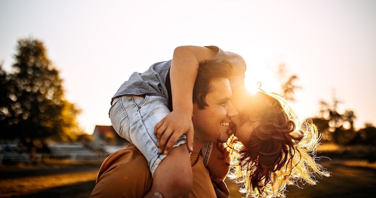 A man is carrying a woman on his back at sunset.
