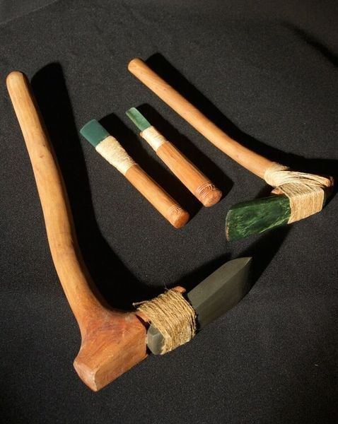 A group of pounamu toki adzes with rimu handles on a black surface