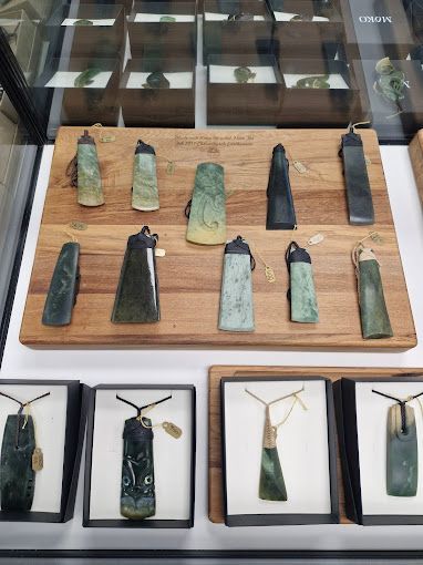 A wooden display case with a variety of pounamu toki pendants