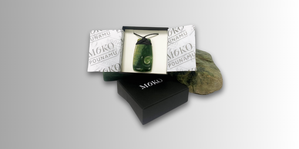 A green pounamu toki pendant sitting inside a black gift box.
