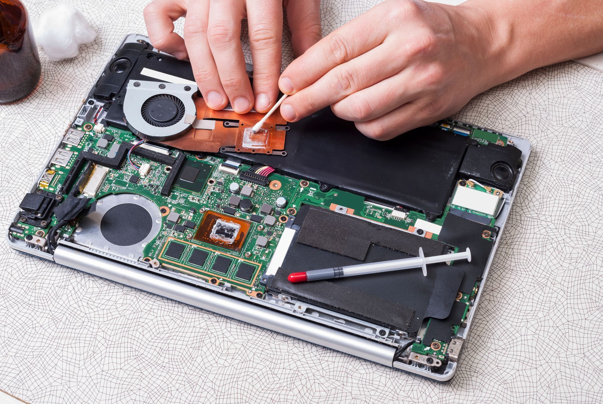 Technician cleaning the internal components of an opened laptop with a cotton swab]