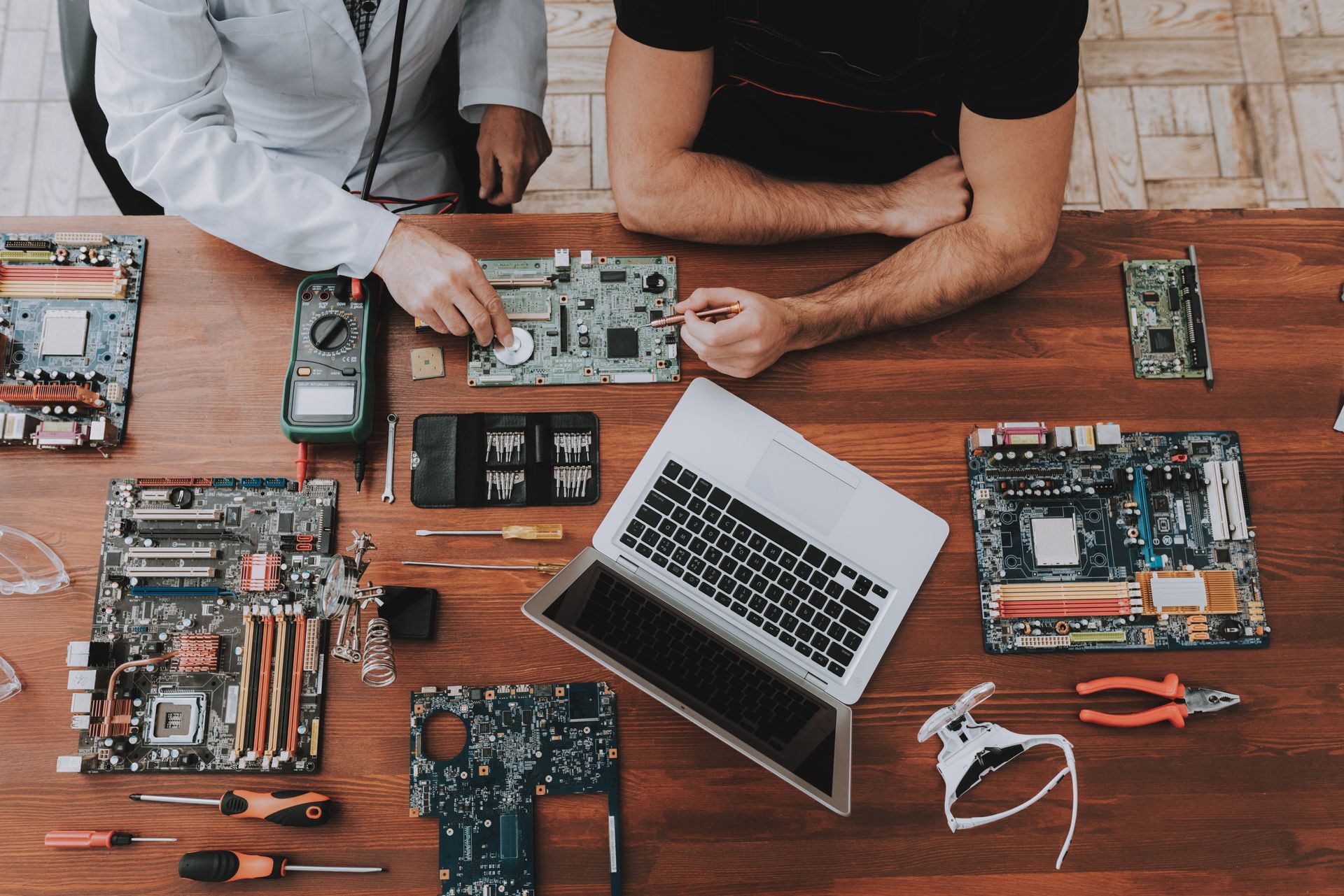 Technicians repairing computer motherboards with tools and a laptop on a workbench