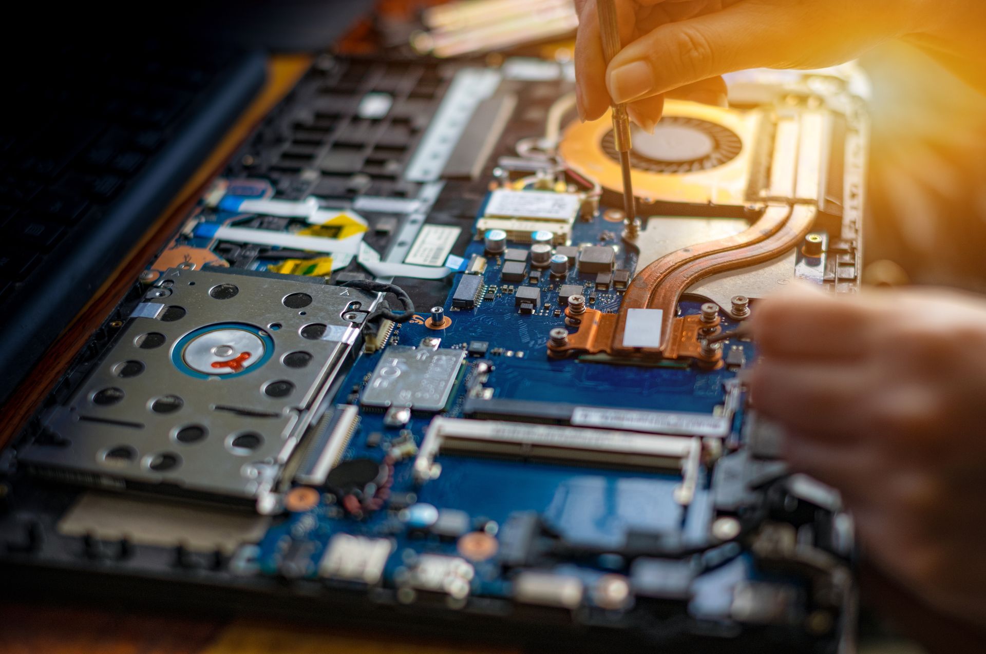Close-up of hands repairing a laptop motherboard with tools and exposed components