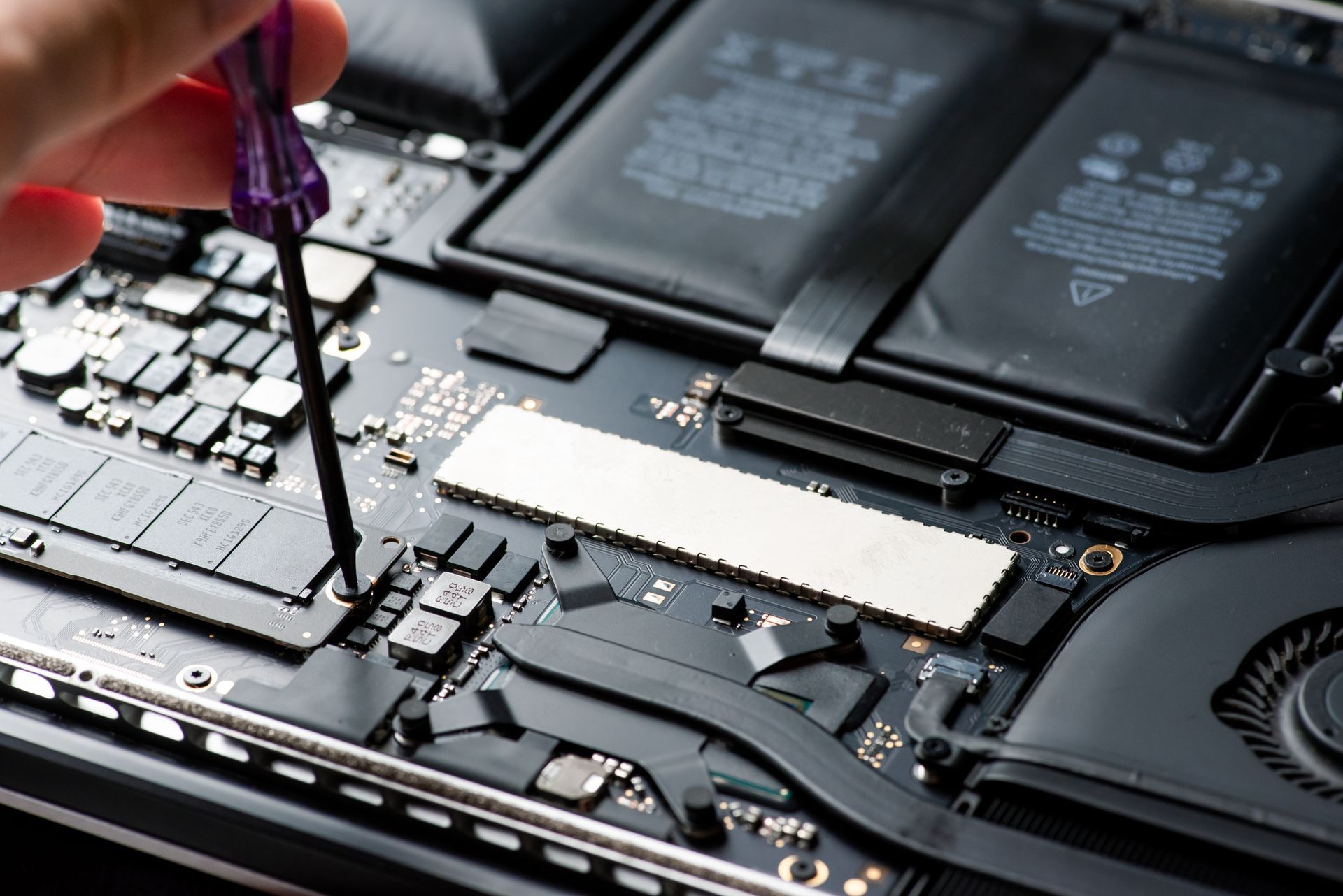 Close-up of a laptop motherboard with a screwdriver working near the battery and internal components