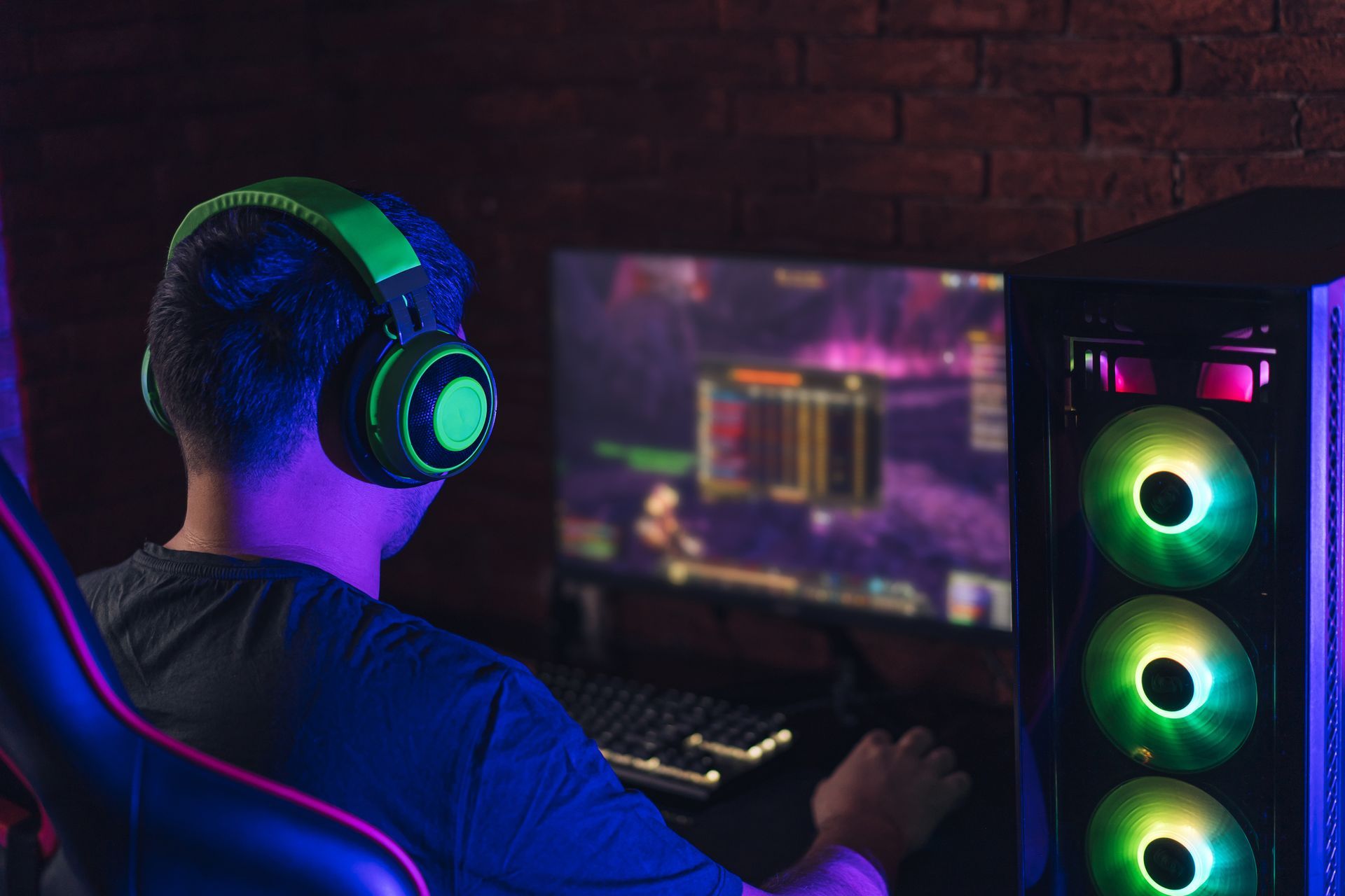 Guy in green headphones playing video games under neon light.