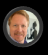 Smiling man with reddish-blond hair in a circular frame, blurry background with figure.