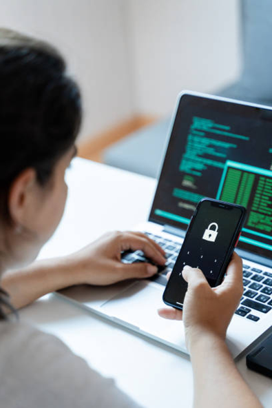 Person using a laptop with a phone displaying a lock icon, suggesting security.
