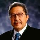 Man with glasses wearing a suit and tie, looking forward.