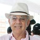 Man wearing a white hat and glasses, smiling. Pink shirt.