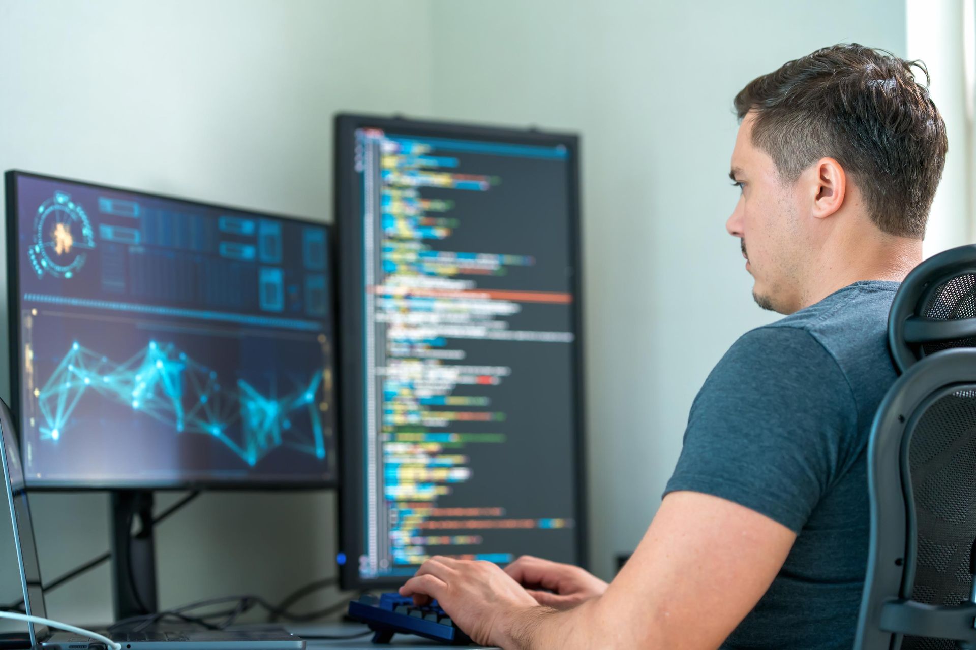 A male programmer immersed in work while facing two computer monitors.
