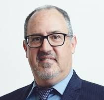Man with glasses and a suit, smiling at the camera.