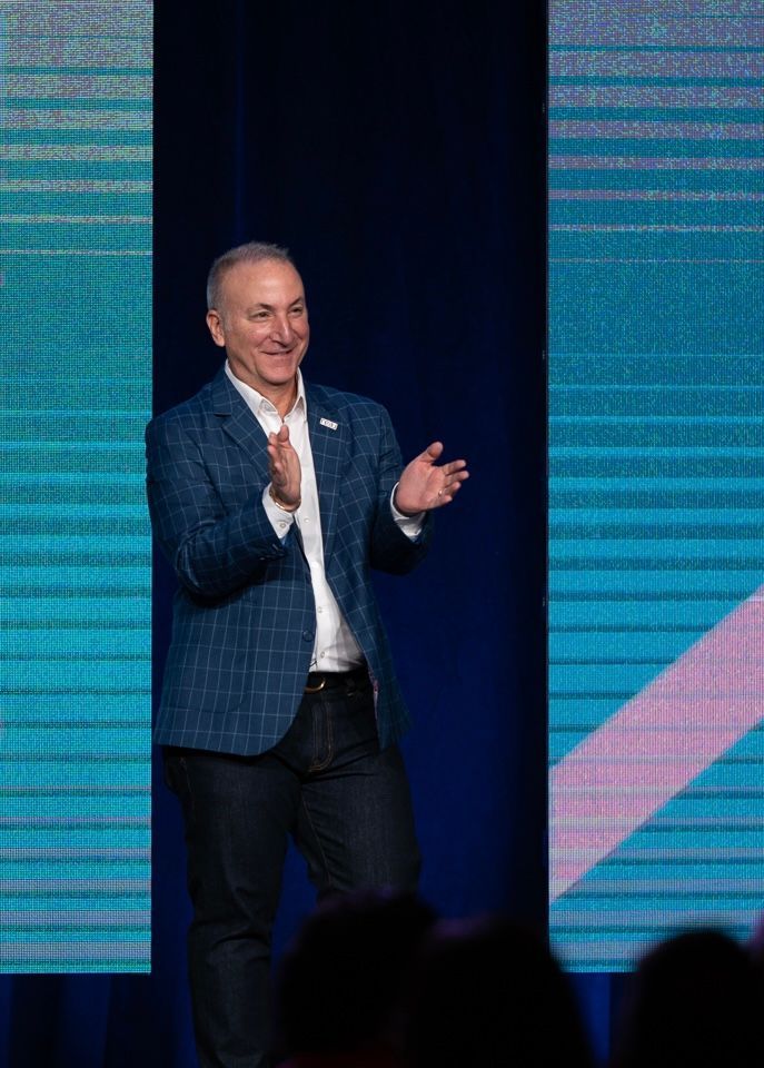 A man in a suit is standing on a stage applauding.