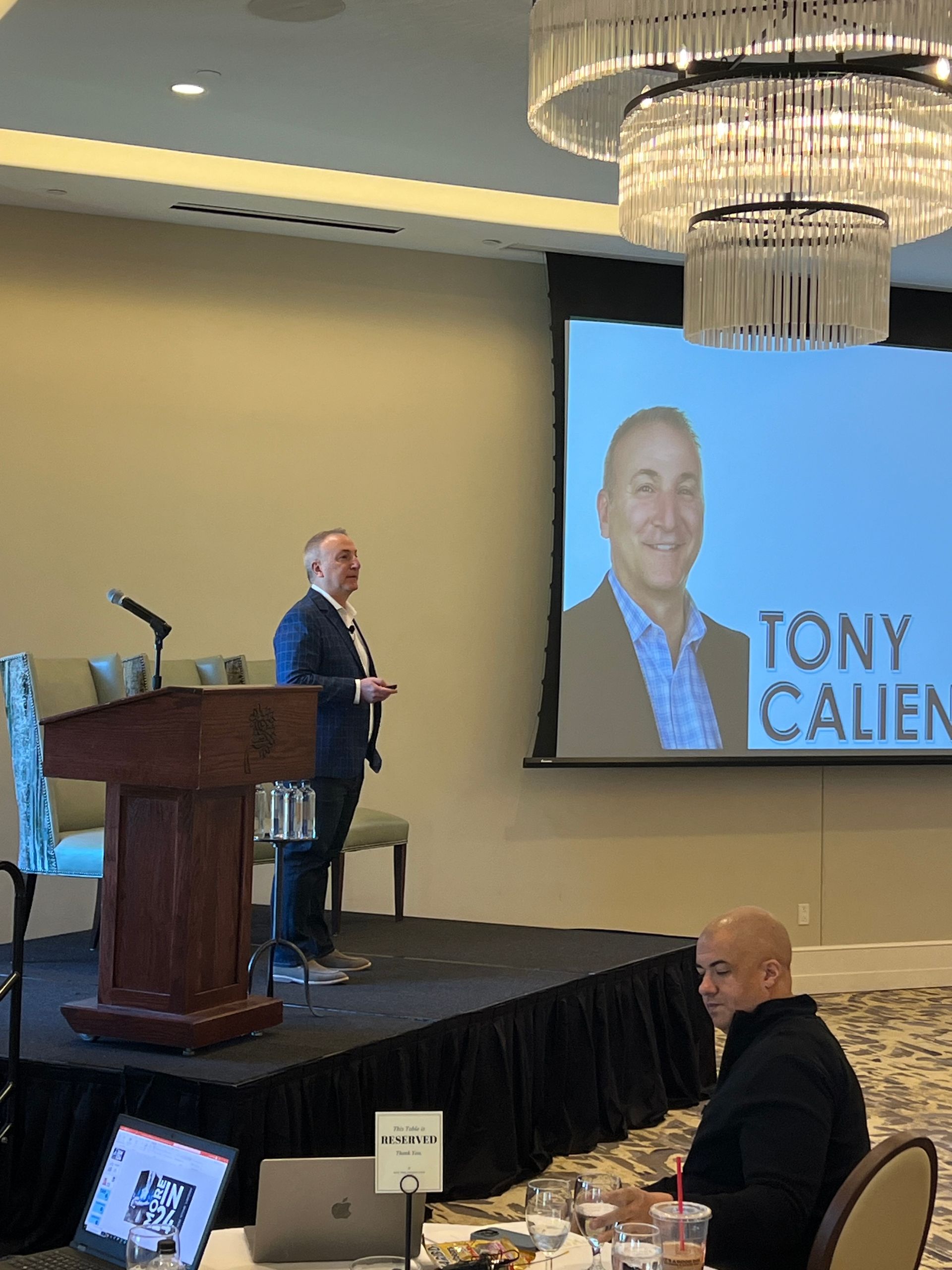A man is giving a speech in front of a screen that says tony calien