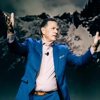 A man in a blue suit is standing with his arms outstretched