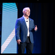 A man in a suit is giving a speech on a stage.