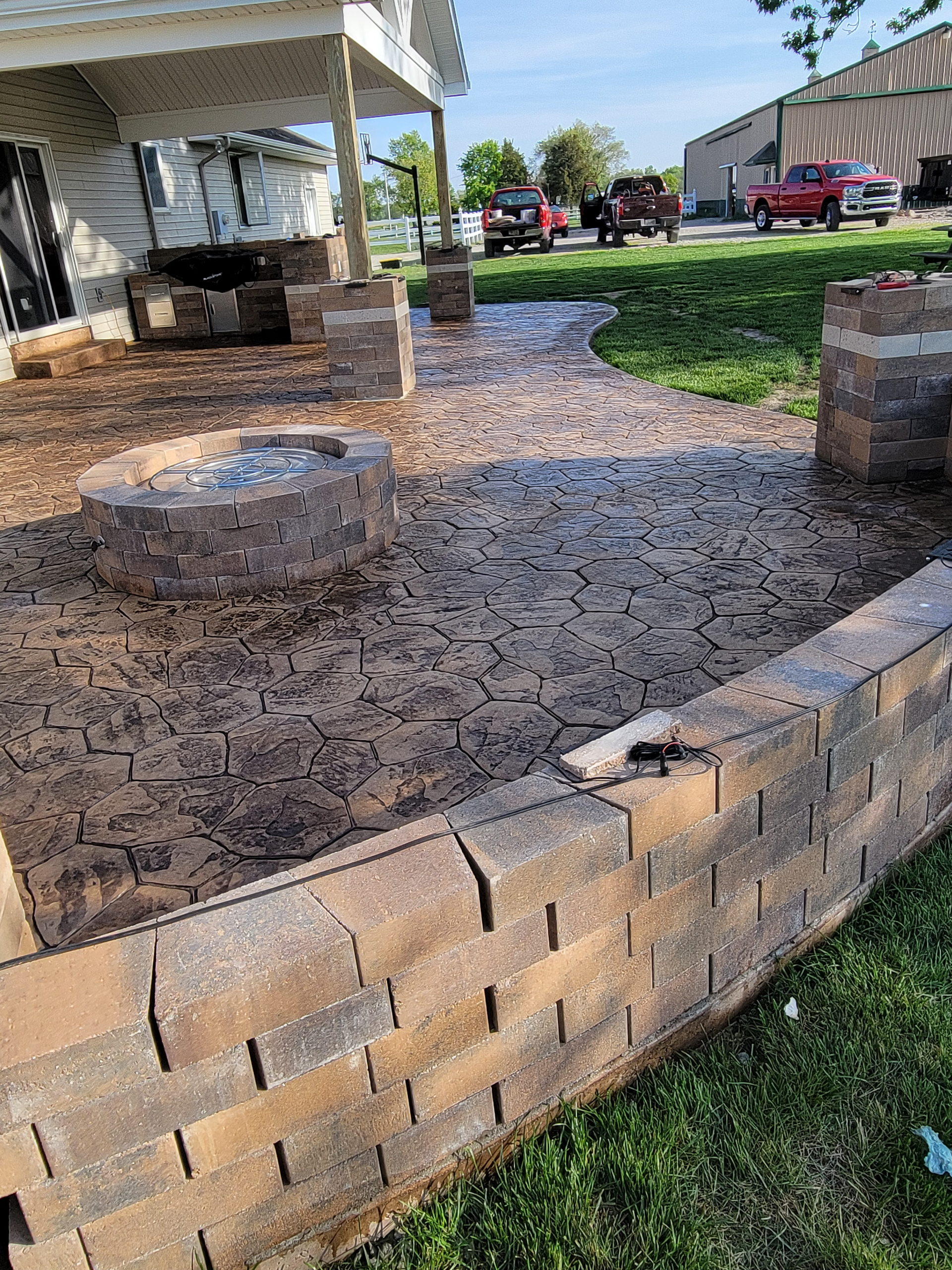 A brick wall is surrounding a patio with a fire pit.