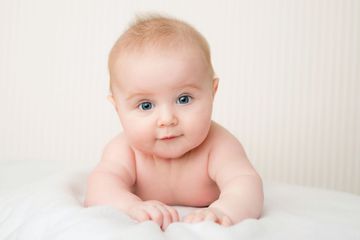 Bambino con pelle chiara e occhi azzurri, sdraiato a pancia in giù su una superficie bianca, con lo sguardo rivolto in avanti.