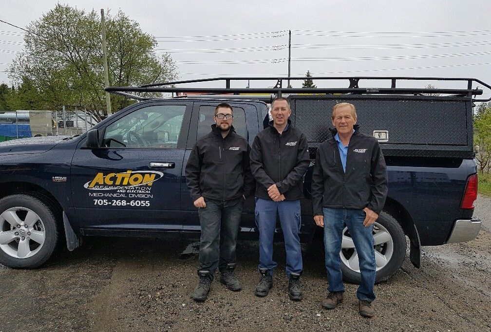 Three men in jackets stand beside a blue truck with 