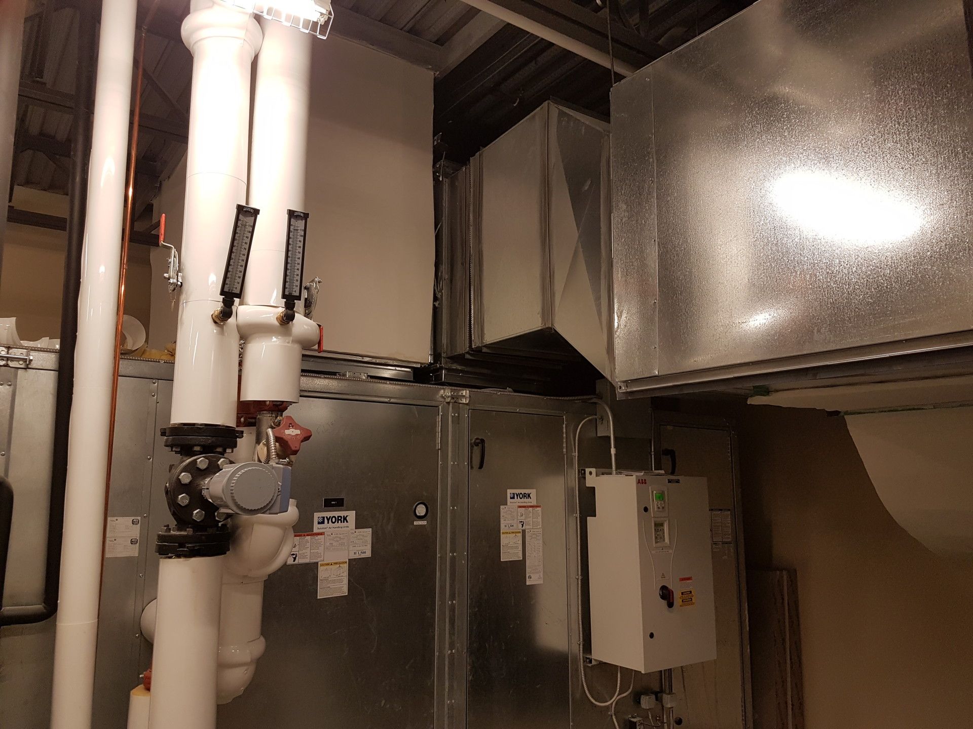 HVAC system with white pipes, silver ducts, and a control panel in an industrial setting.