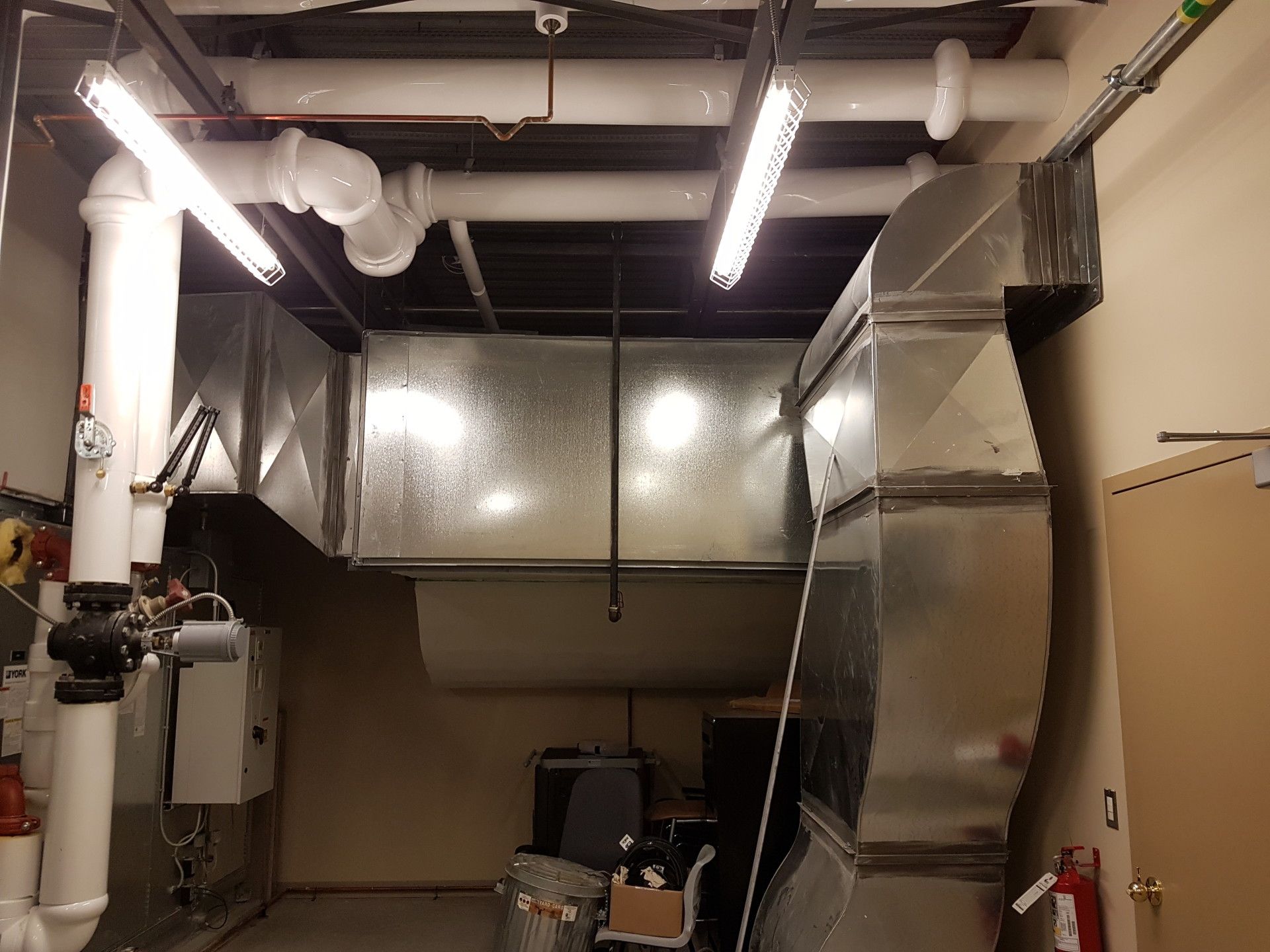 HVAC system with ductwork, pipes, and lighting in a utility room.