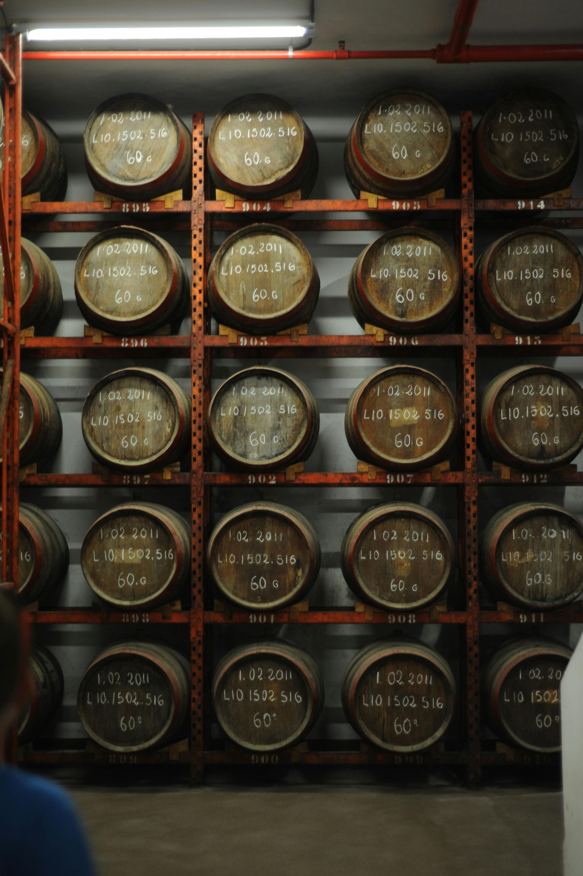 A storage rack filled with rows of wooden wine or spirit barrels in a dimly lit, industrial cellar setting.