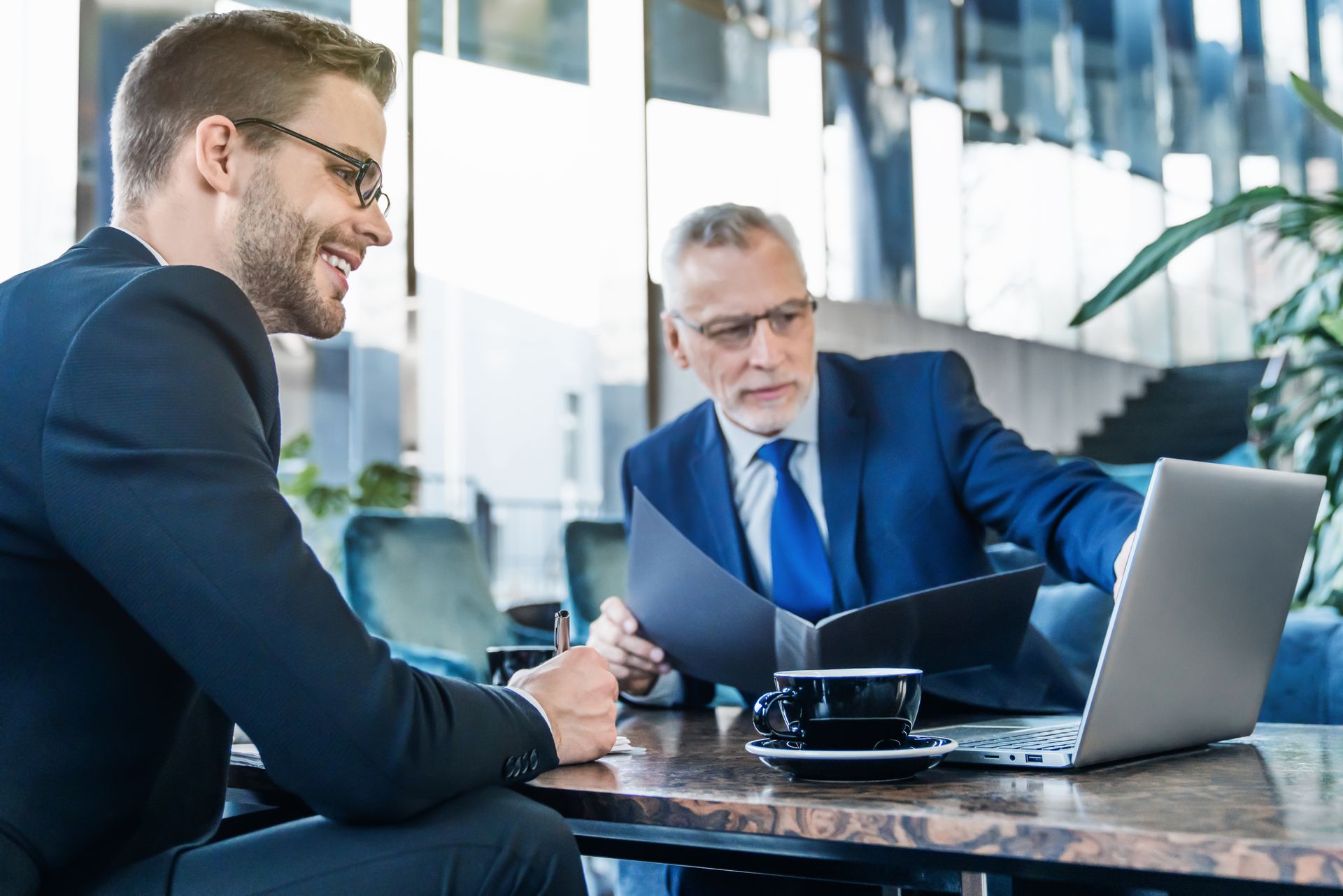 Two businessmen in suits discussing over a laptop at a modern office table