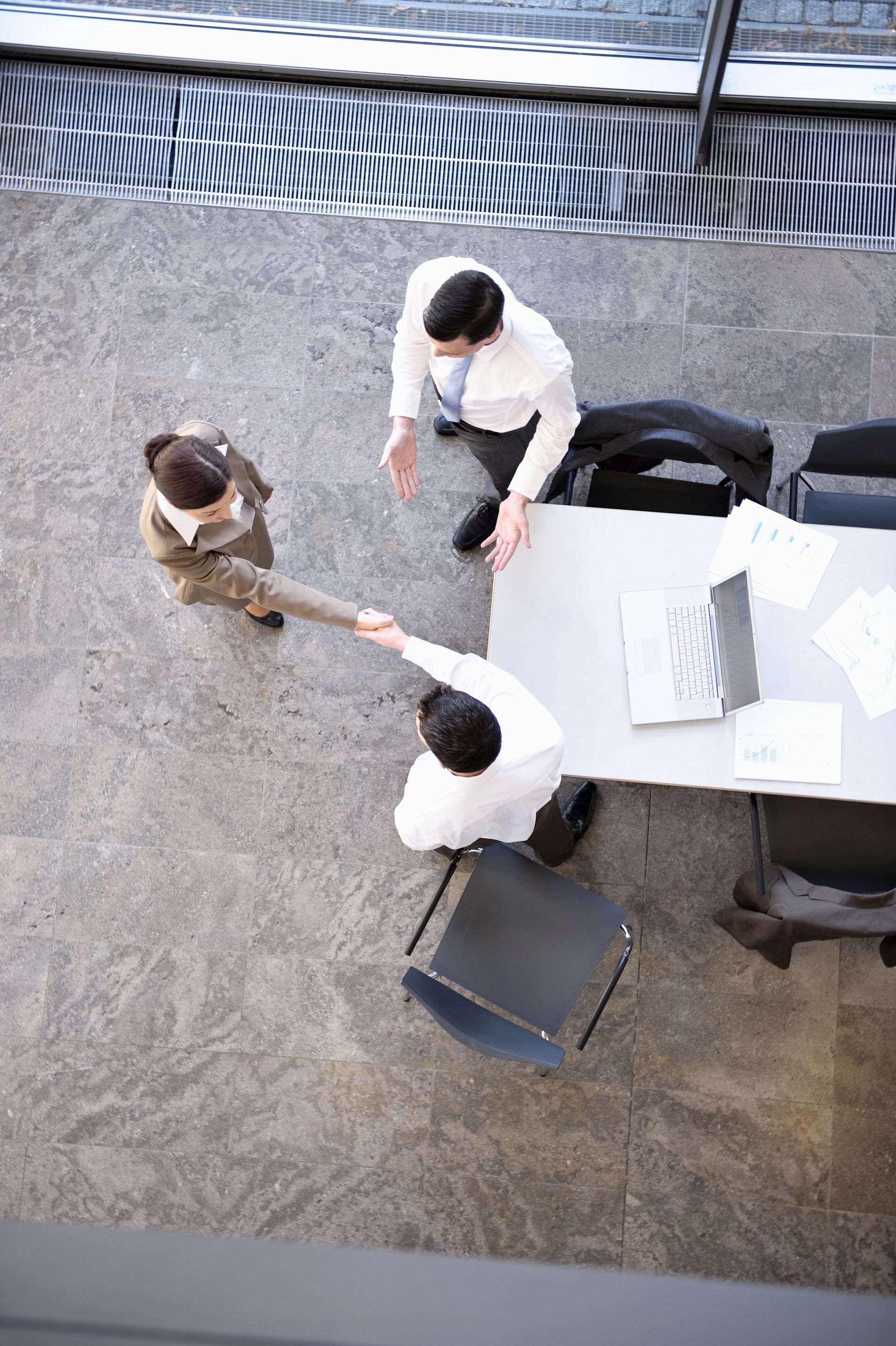 Three people gathered around a white table in a courtyard, reaching toward each other in conversation.