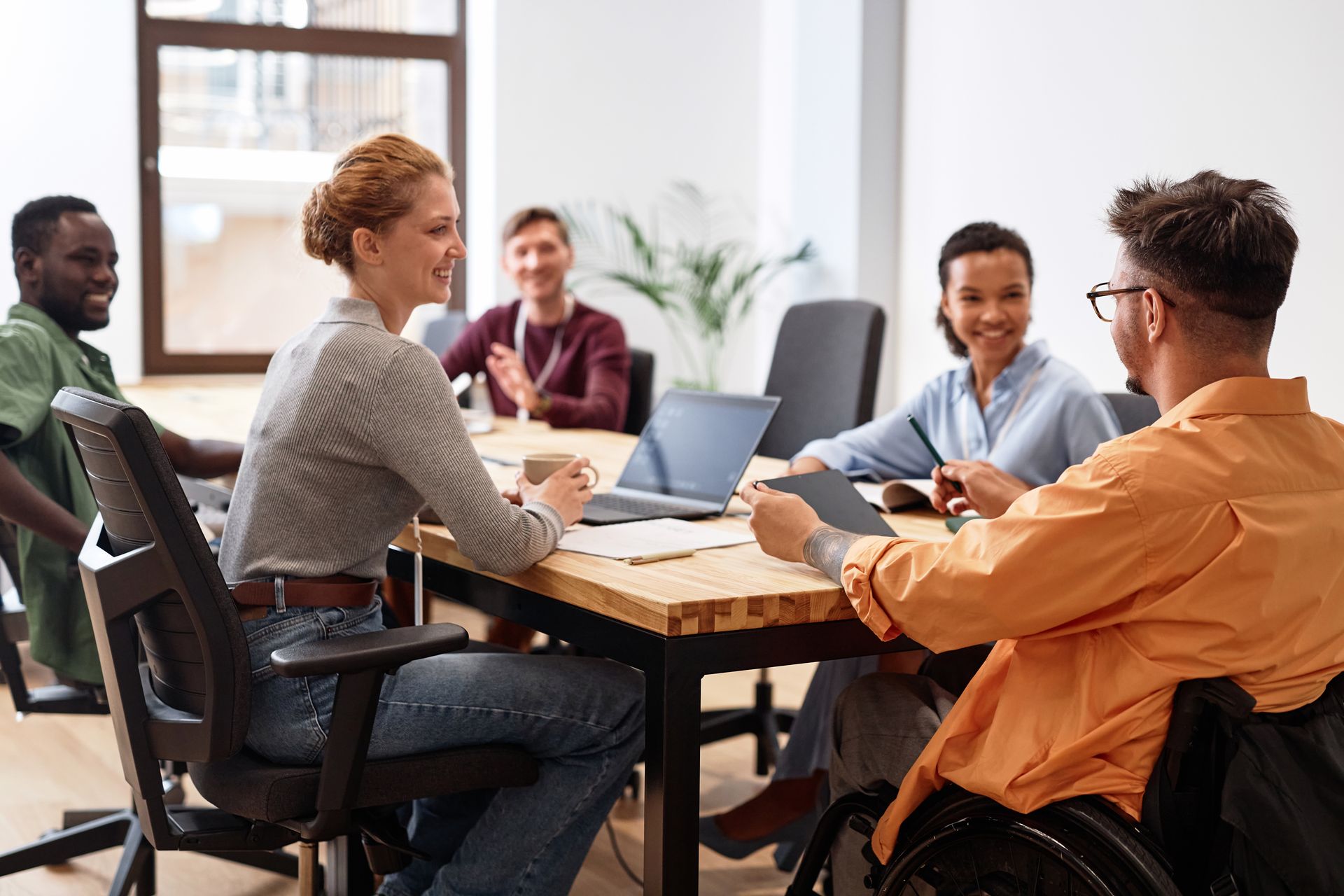 Team meeting around a wooden table in a bright office, with laptops and notebooks open.