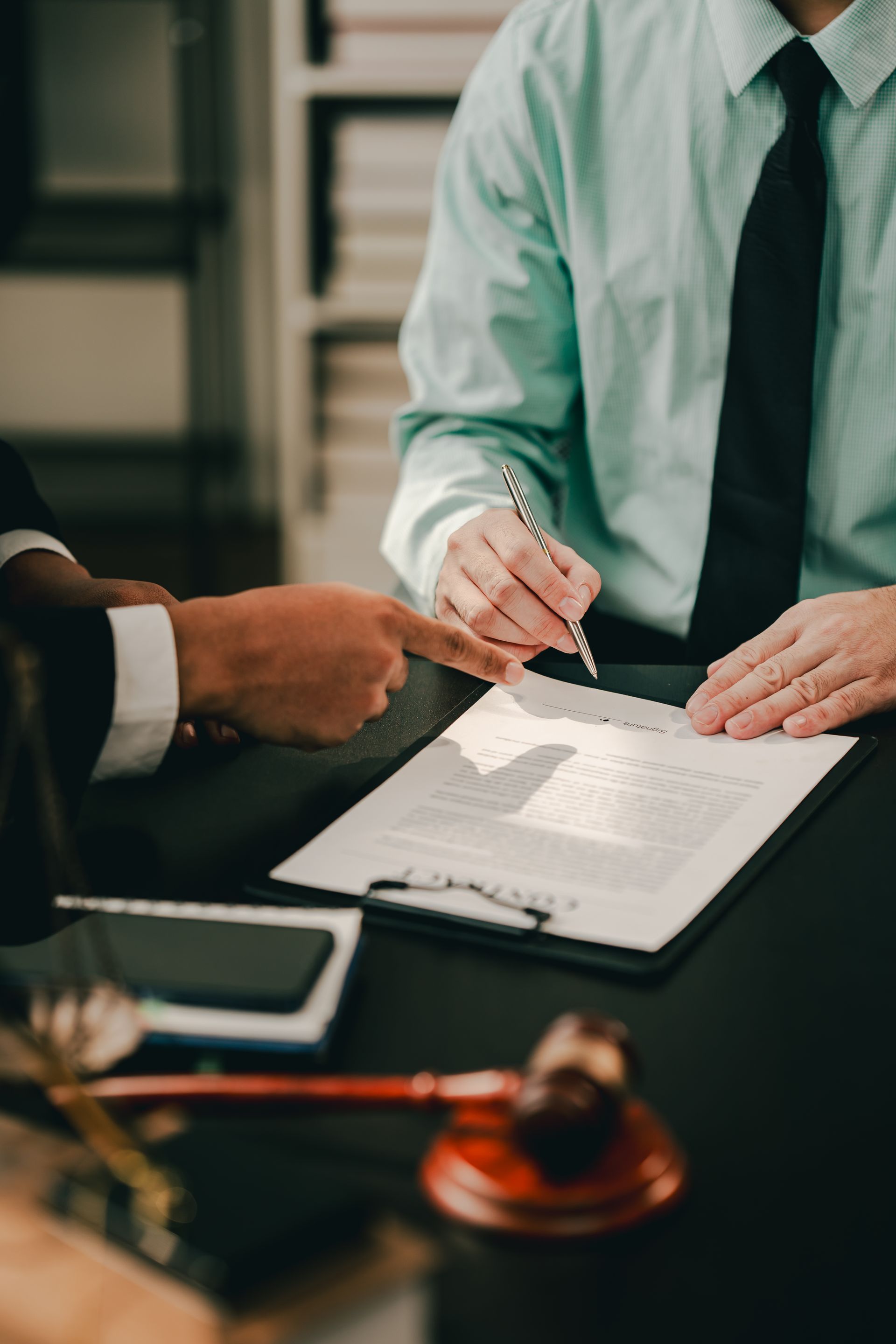 Two people signing a document at a desk, with a judge’s gavel nearby