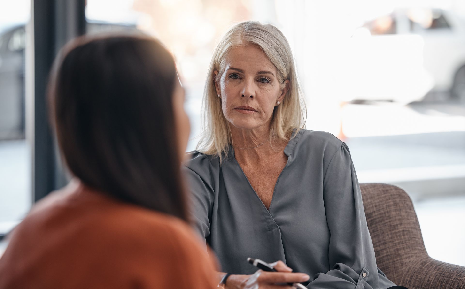 Two women in conversation in a bright office, one facing the camera with a thoughtful expression.