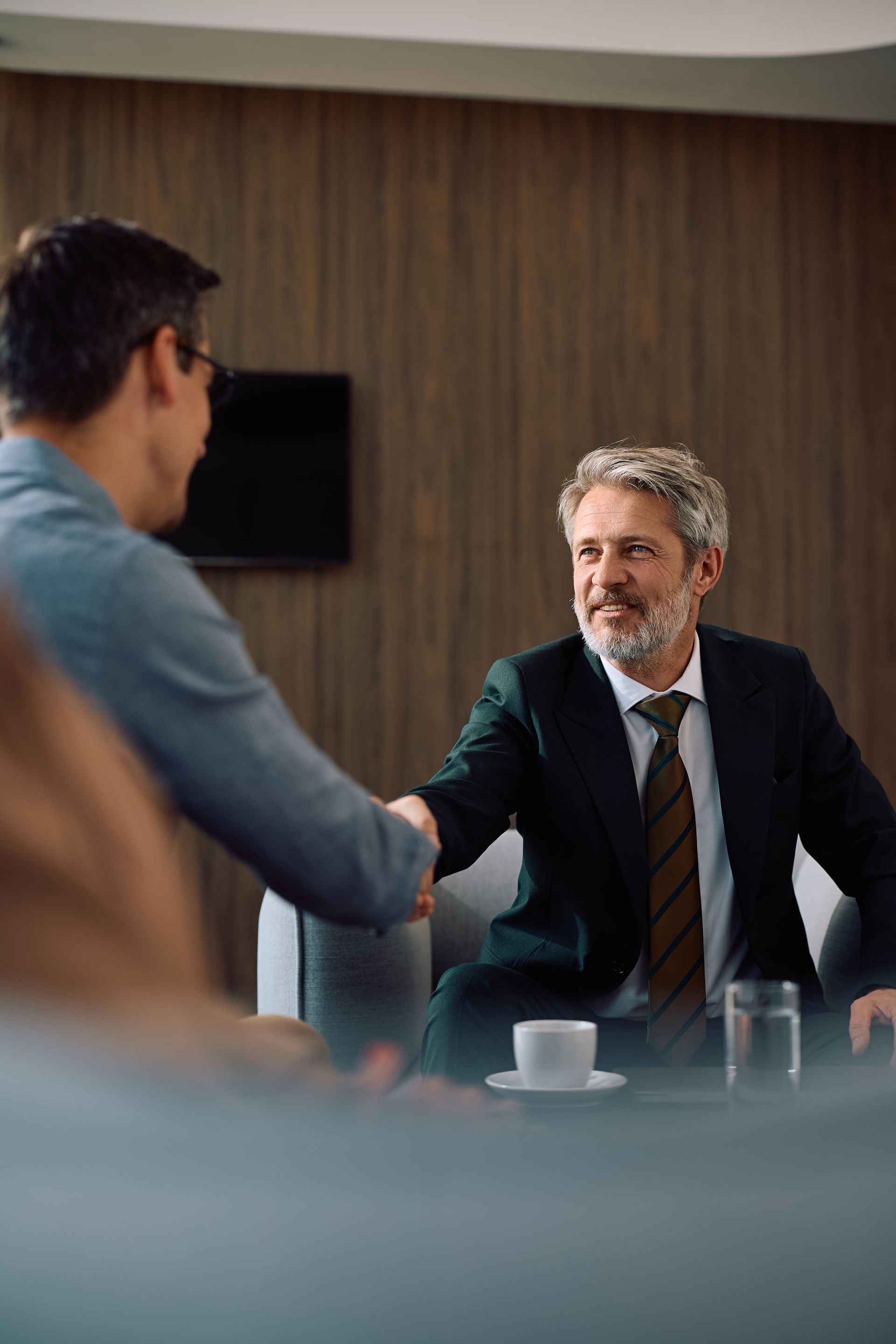 Two men shake hands across a conference table in a modern meeting room.