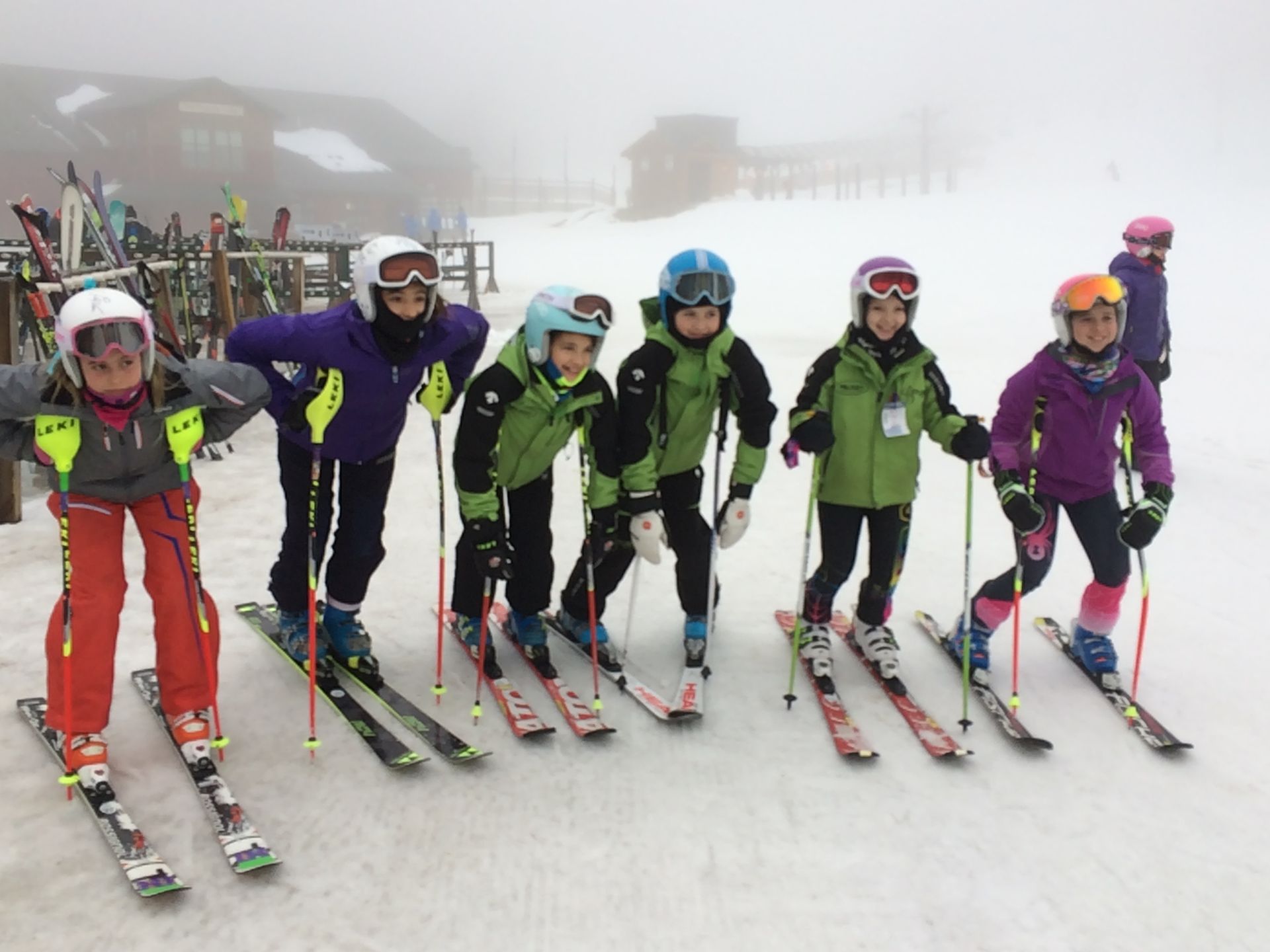 Group of skiers in colorful gear standing on snow, ready to ski, with a foggy backdrop.