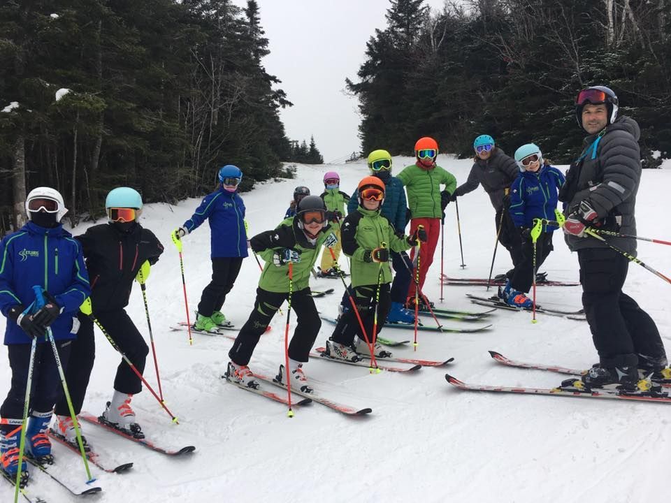 Group of skiers on a snow-covered slope, getting ready to ski down. Ski poles and colorful jackets are visible.