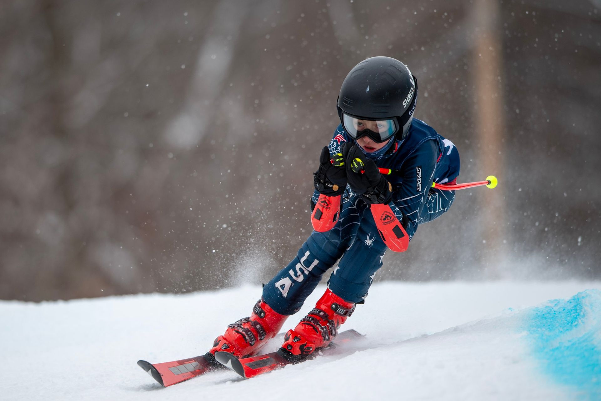 Skier carving down a snow-covered slope, creating a blue trail of snow. Red boots, helmet.