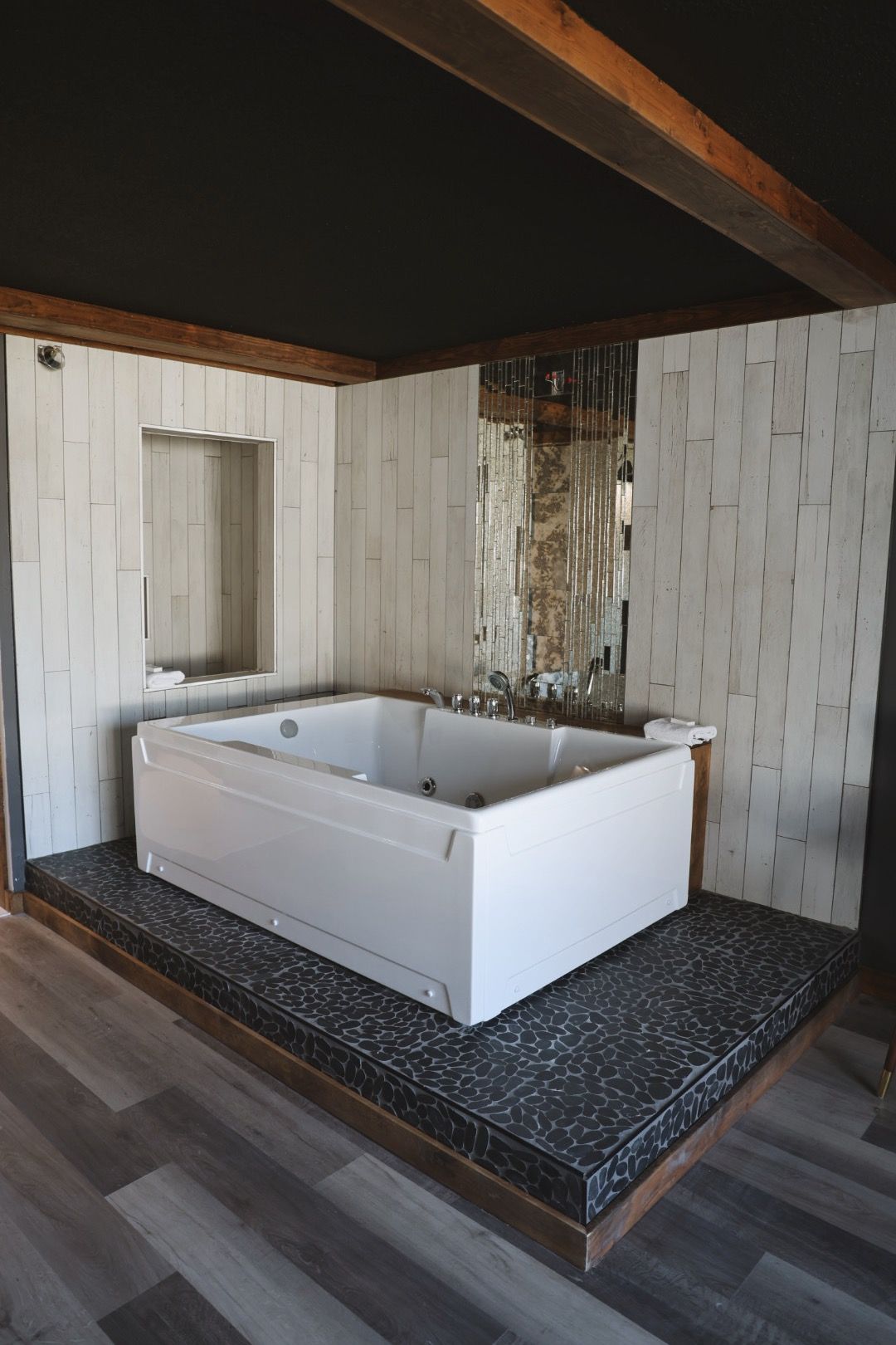 A large white bathtub is sitting on top of a wooden platform in a bathroom.