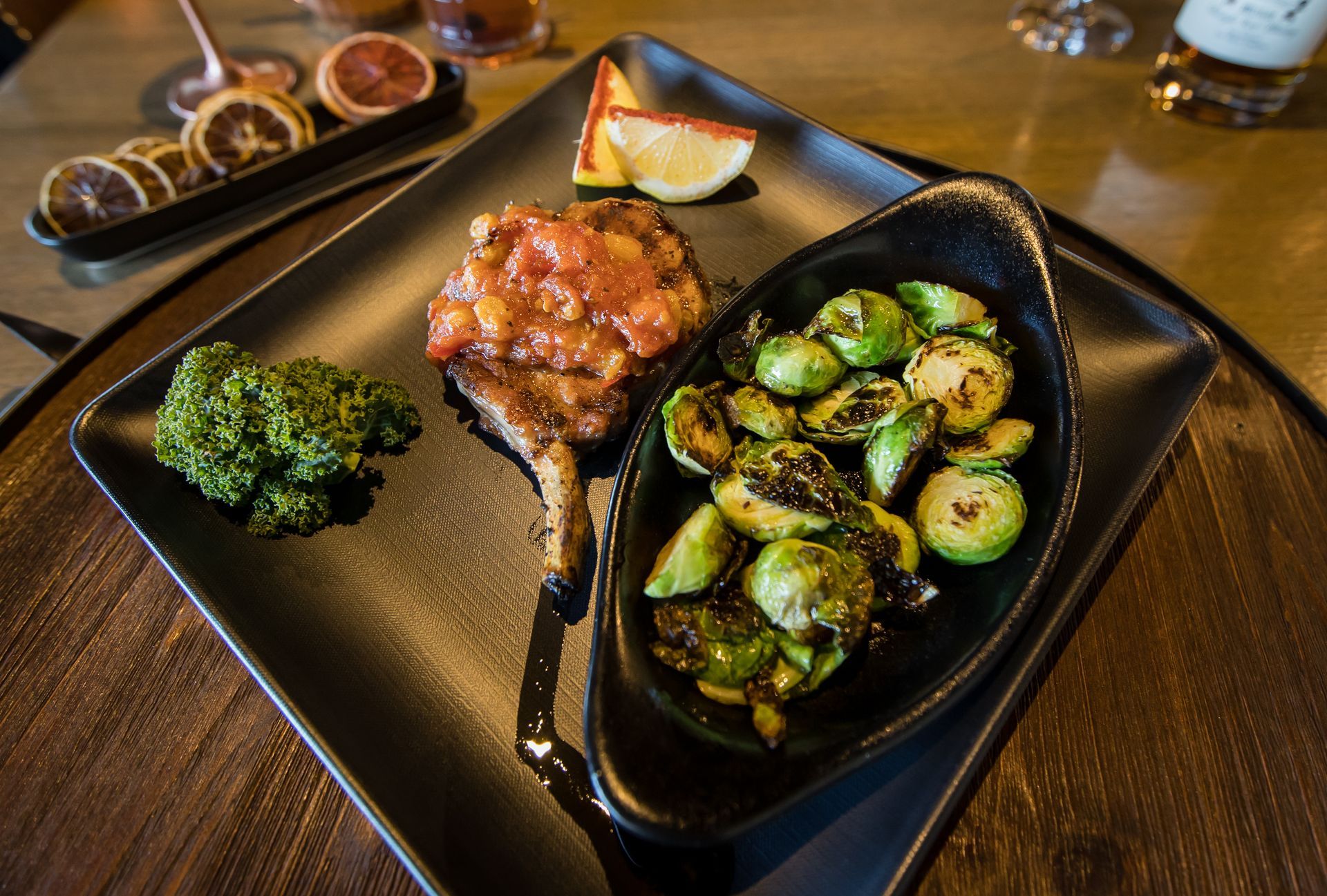 A black plate topped with meat and vegetables on a wooden table.