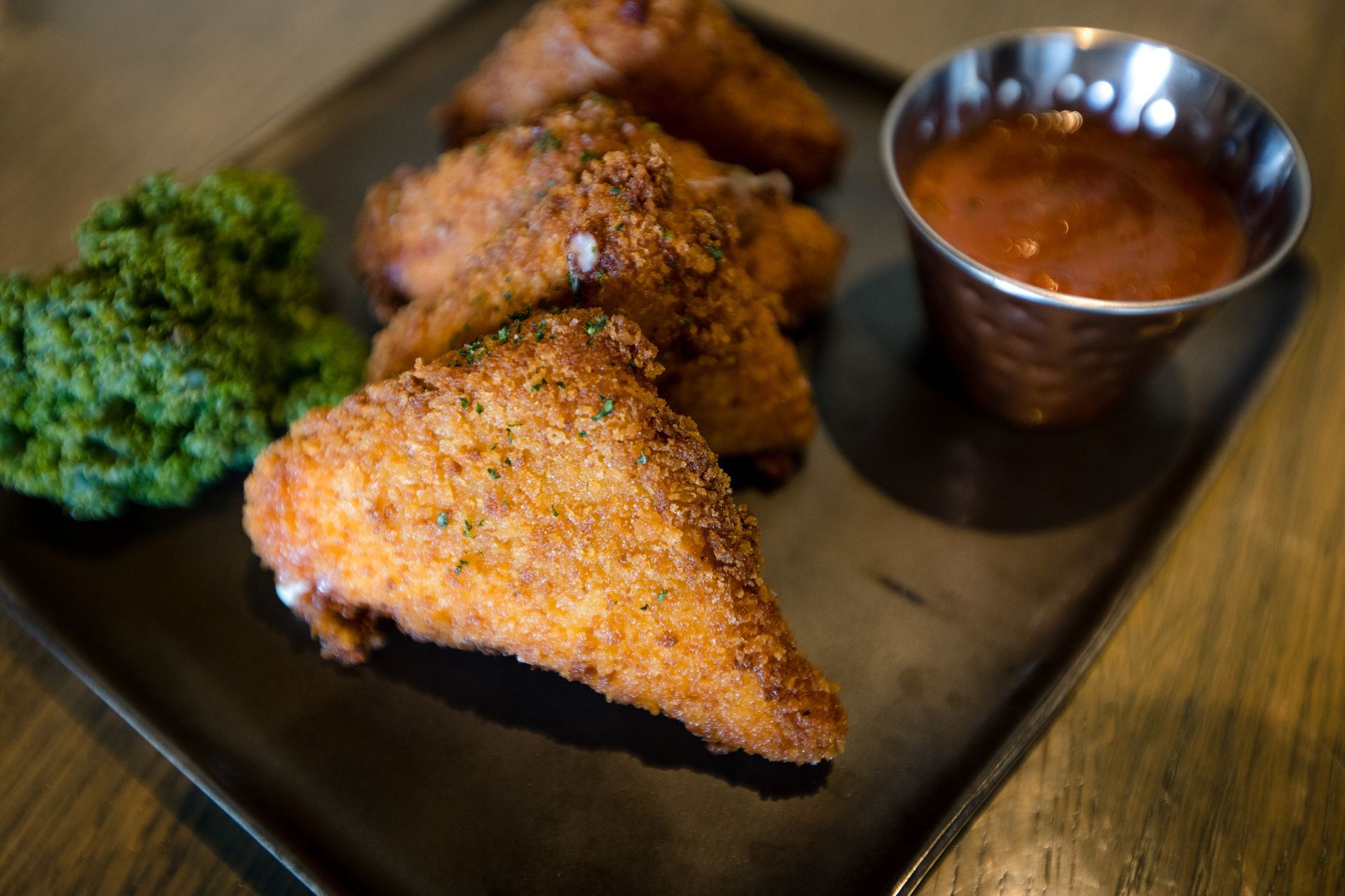A black plate topped with fried chicken wings and a dipping sauce.