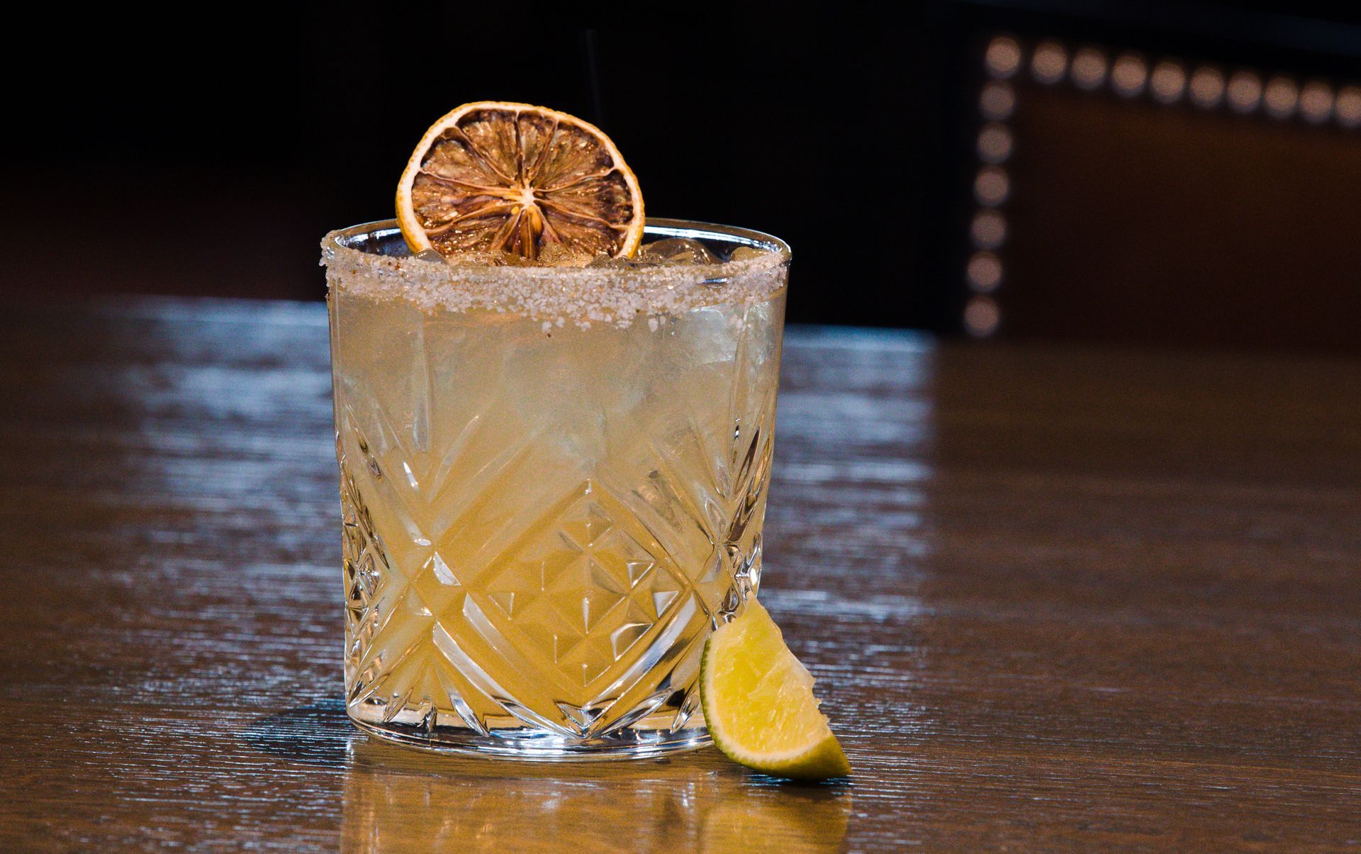 A drink in a glass with a slice of lemon on top of it on a table.