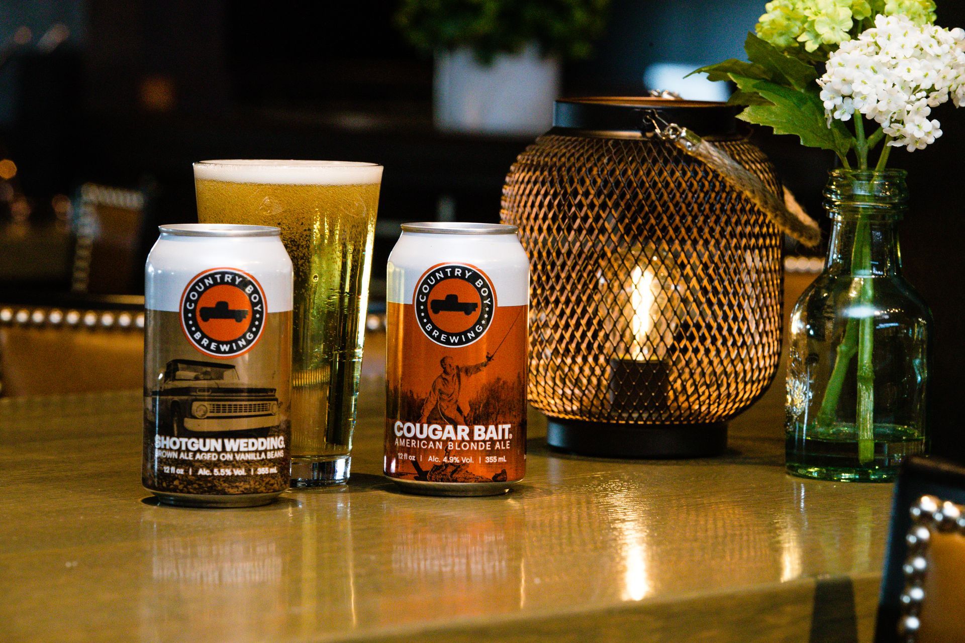 Three cans of beer are sitting on a counter next to a glass of beer.