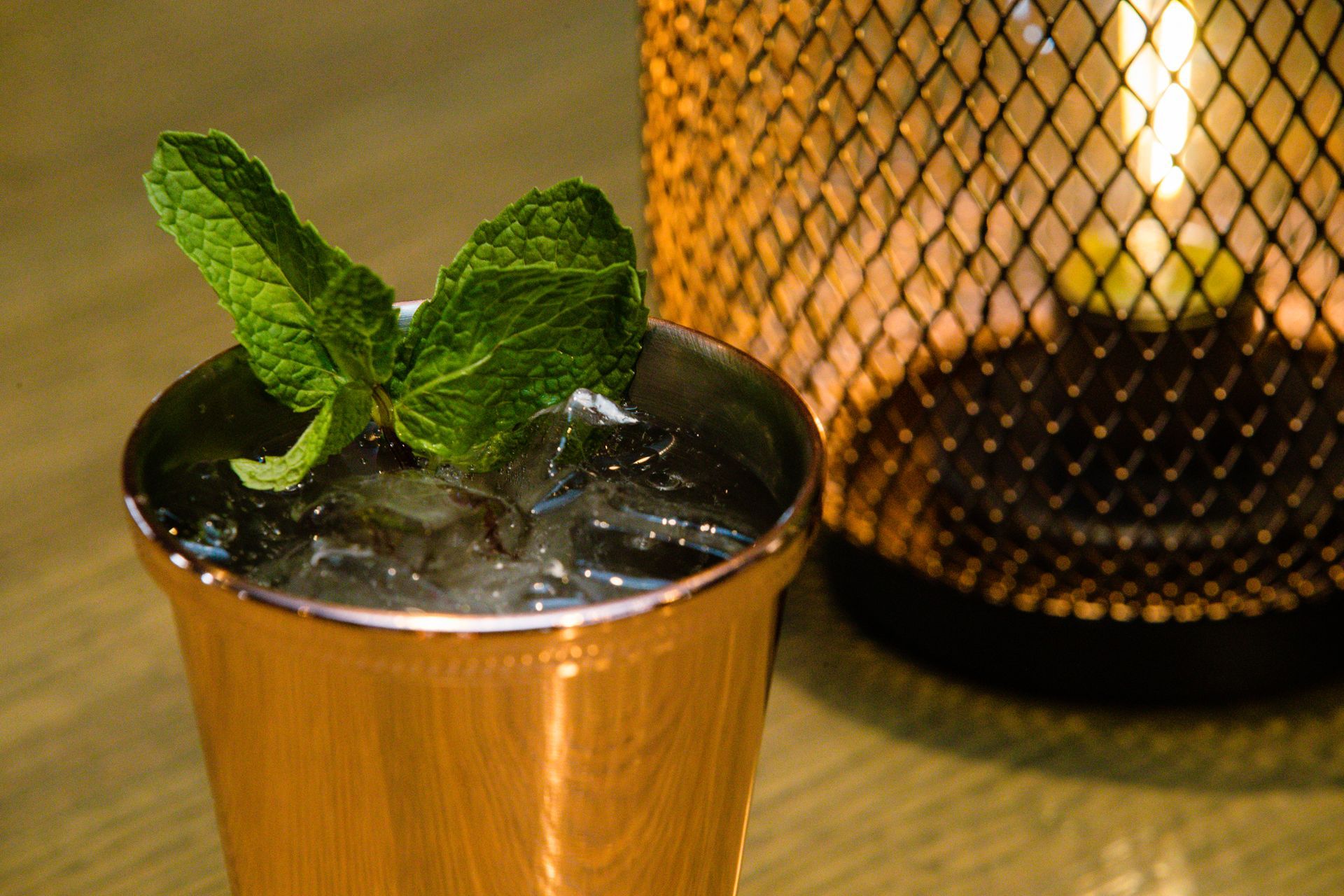 A copper cup filled with ice and mint leaves next to a candle holder.