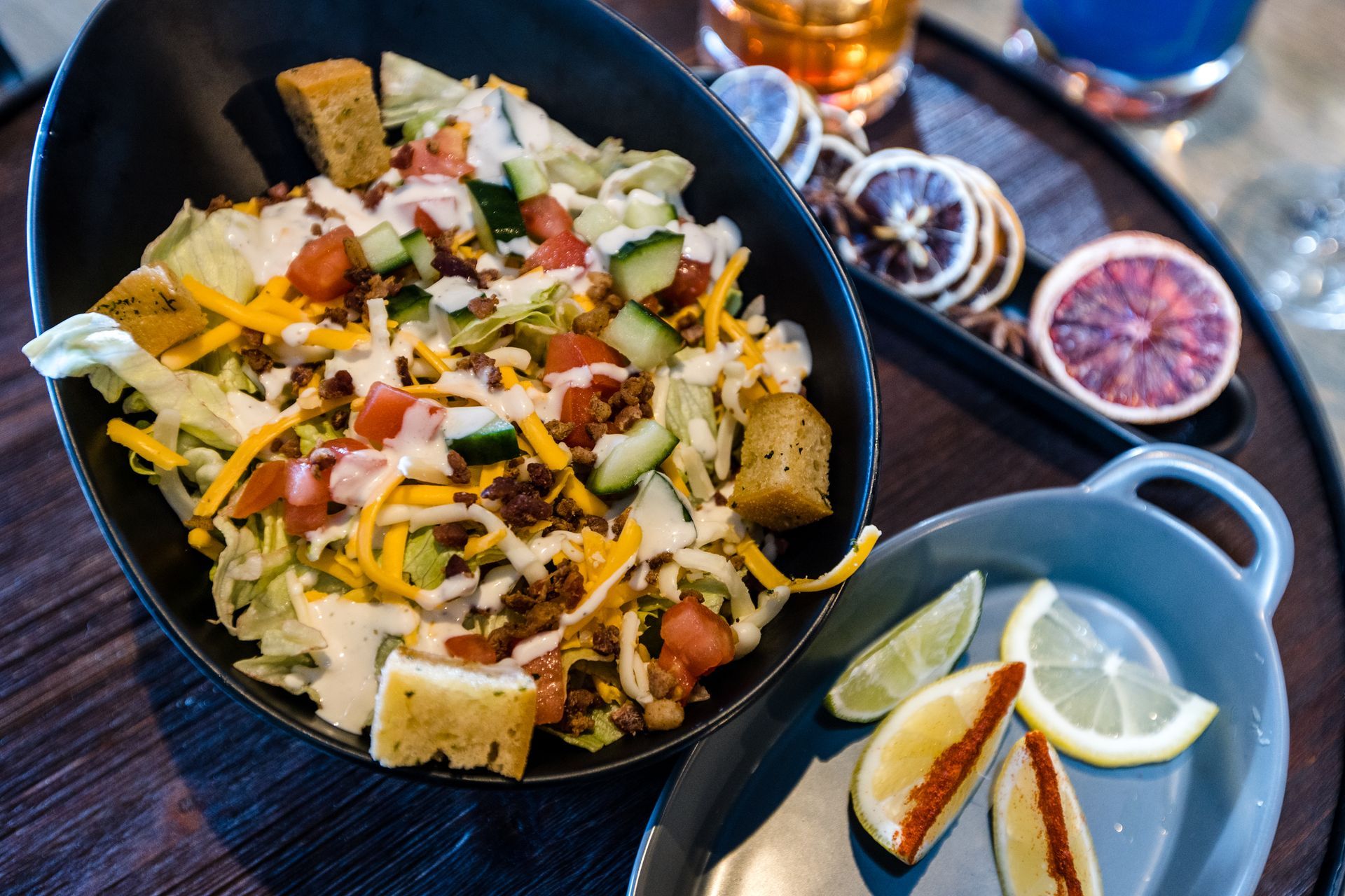 A salad in a bowl on a table next to a plate of lemon slices.