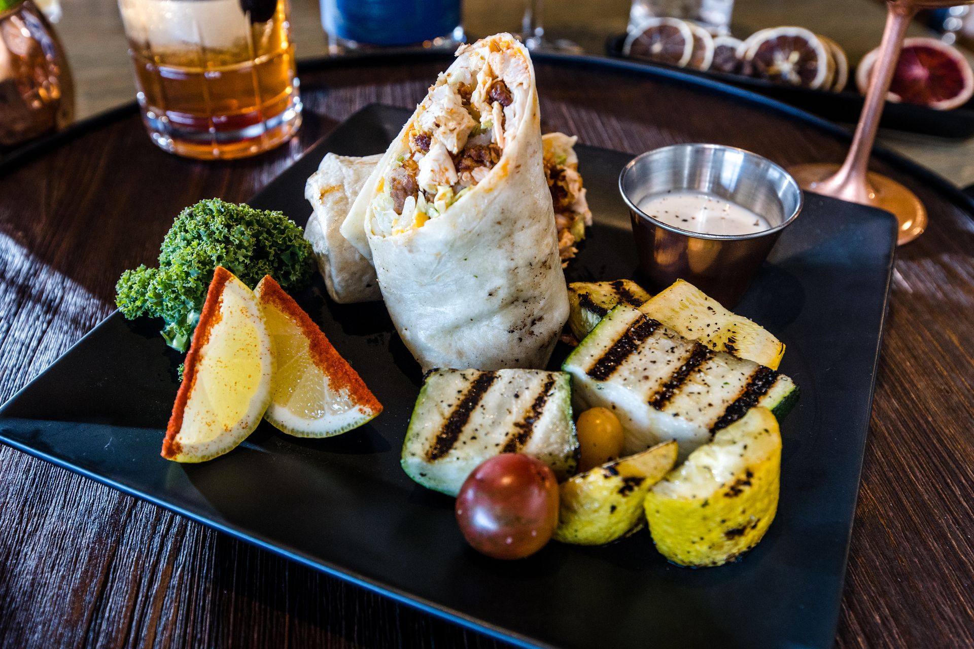 A burrito with vegetables on a black plate on a table.