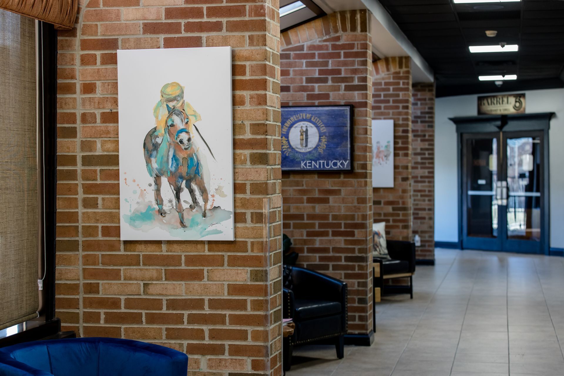 A painting of a jockey riding a horse is hanging on a brick wall.