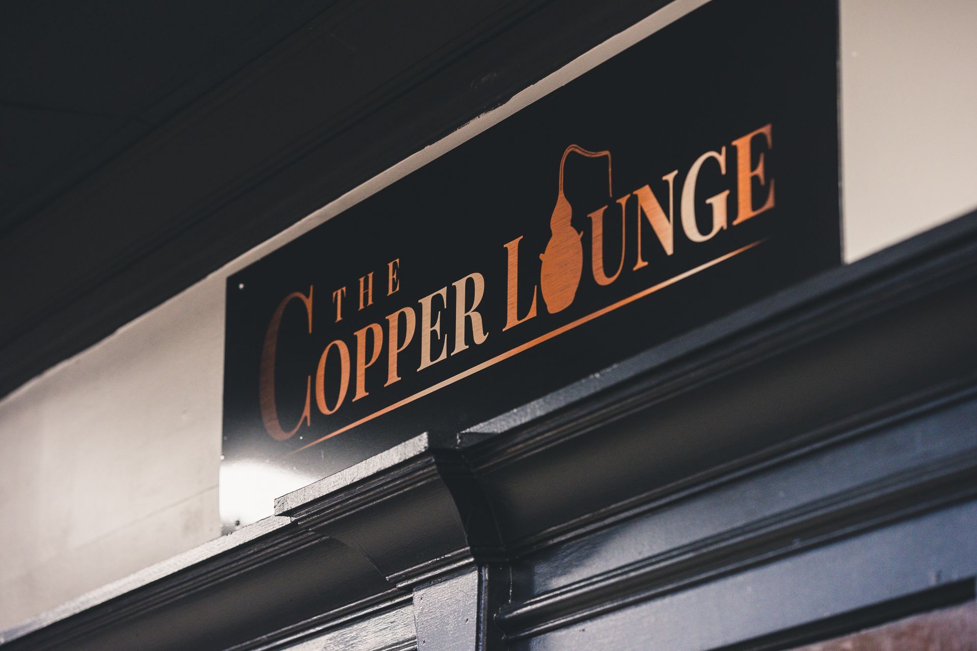 A sign for the copper lounge is on the side of a building.