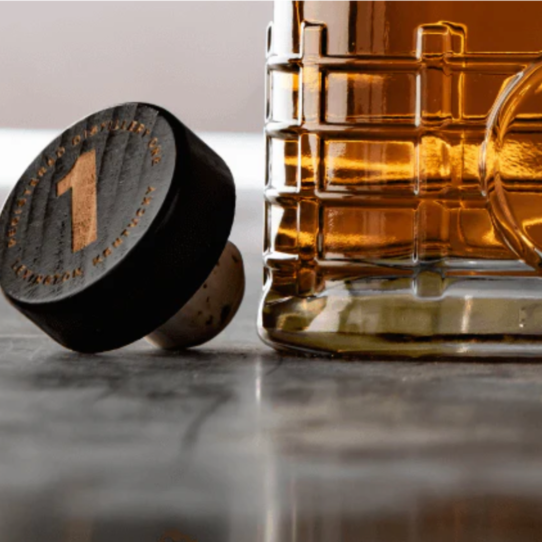 A close up of a glass of whiskey and a cork on a table.