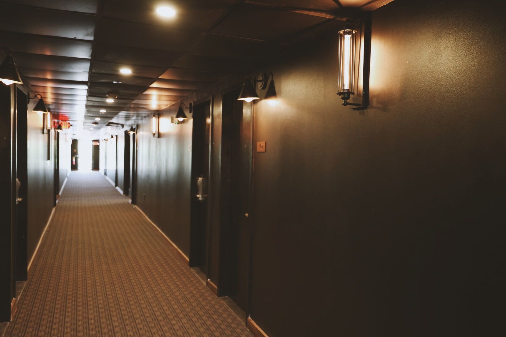 A long hallway in a hotel with a lot of doors and lights on the walls.
