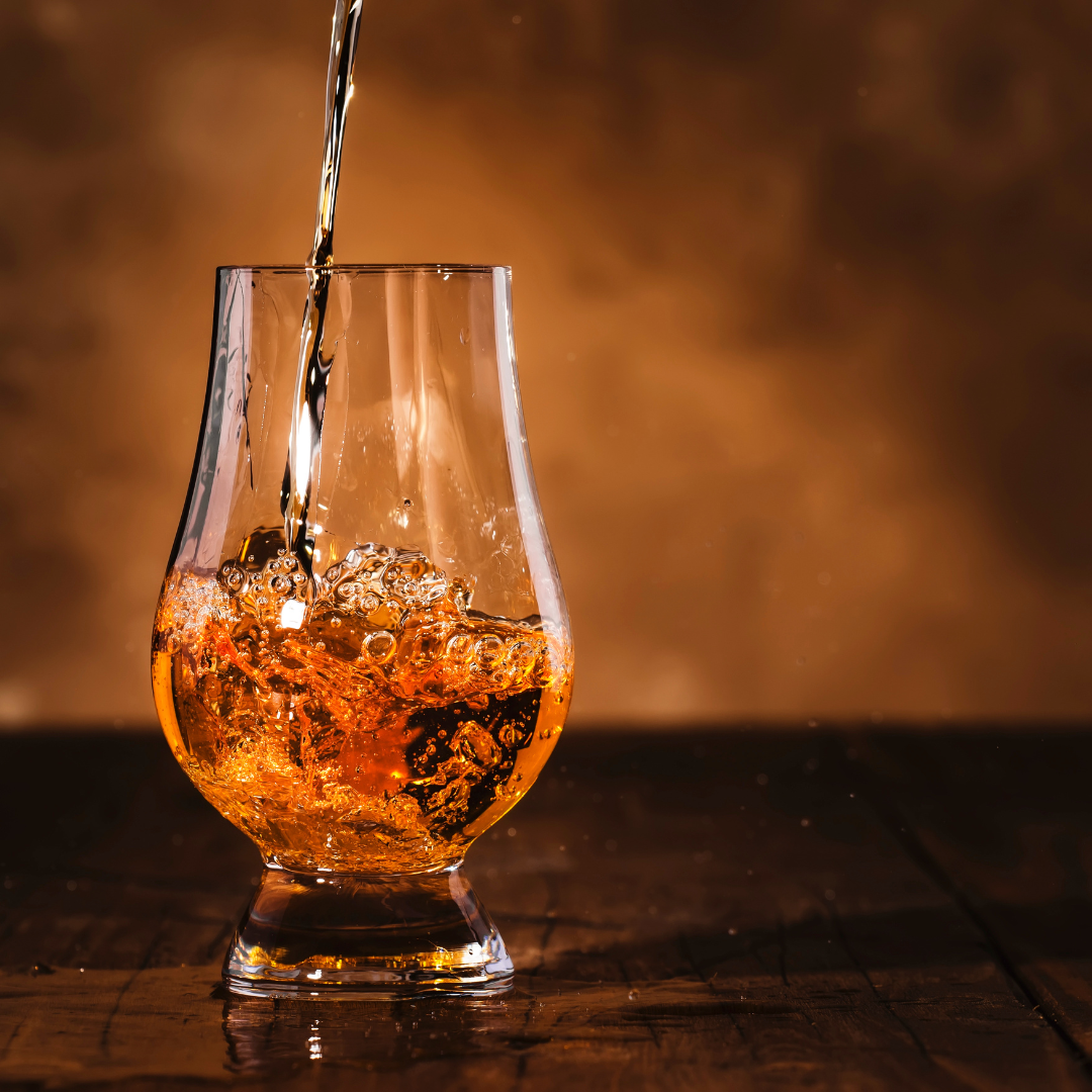 A glass of whiskey is being poured into a glass on a wooden table.