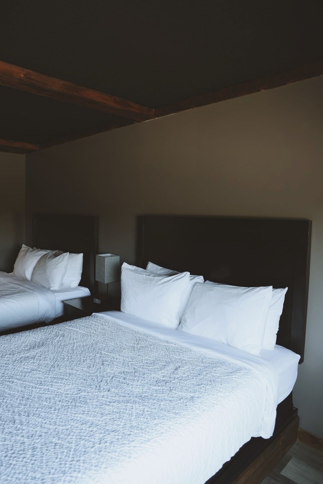 There are two beds in the room with white sheets and pillows.