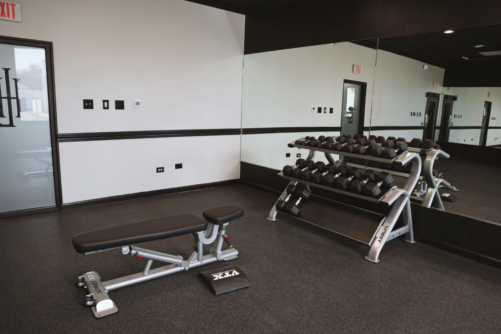 A gym with a bench and dumbbells in front of a large mirror.