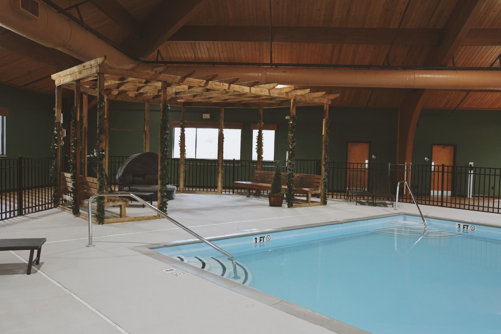 An indoor swimming pool with a pergola and chairs in a building.